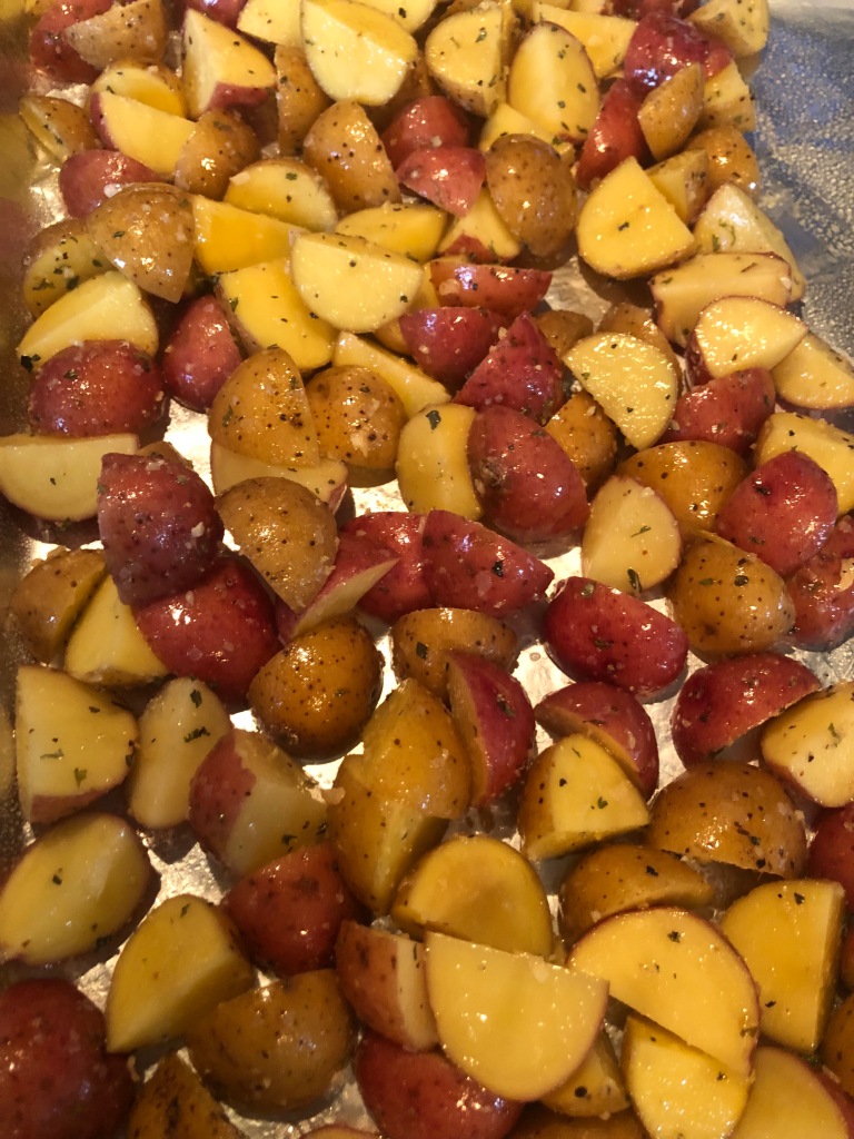 Quartered baby potatoes mixed with salt, parmesan cheese and herbs on foil-covered sheet pan, ready to roast.